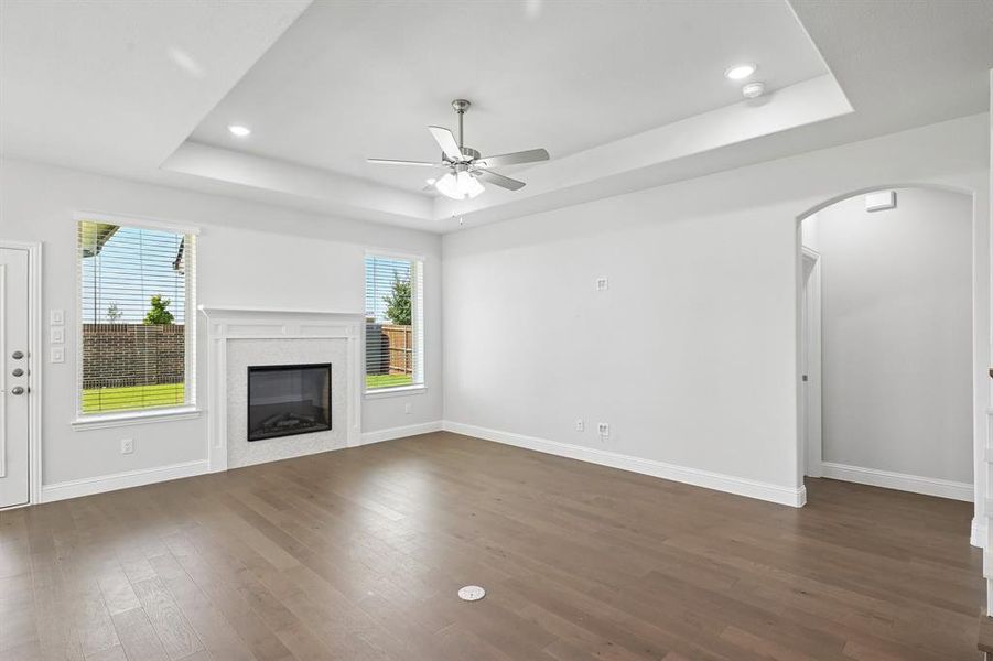 Living area featuring a tray ceiling with recessed lighting, a ceiling fan, and wood-finish flooring Living area featuring a tray ceiling with recessed lighting, a ceiling fan, and wood-finish flooring