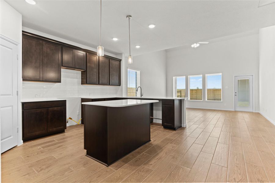 Gorgeous gourmet kitchen showcasing stunning granite countertops, tall shaker style cabinets, stainless steel appliances, gas cooking, and a spacious center island perfect for meal preparation or casual dining. The beautiful wood looking tile flooring flows seamlessly throughout the kitchen and main living areas, creating a warm and elegant atmosphere.