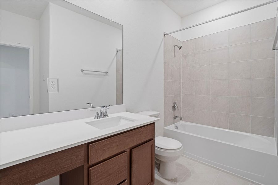 The secondary bathroom offers tile flooring, a bath/shower combination with a stylish tile surround, rich stained wood cabinetry with added knee space and elegant light countertops, a mirror, and sleek fixtures with modern finishes. The secondary bathroom offers tile flooring, a bath/shower combination with a stylish tile surround, rich stained wood cabinetry with added knee space and elegant light countertops, a mirror, and sleek fixtures with modern finishes.
