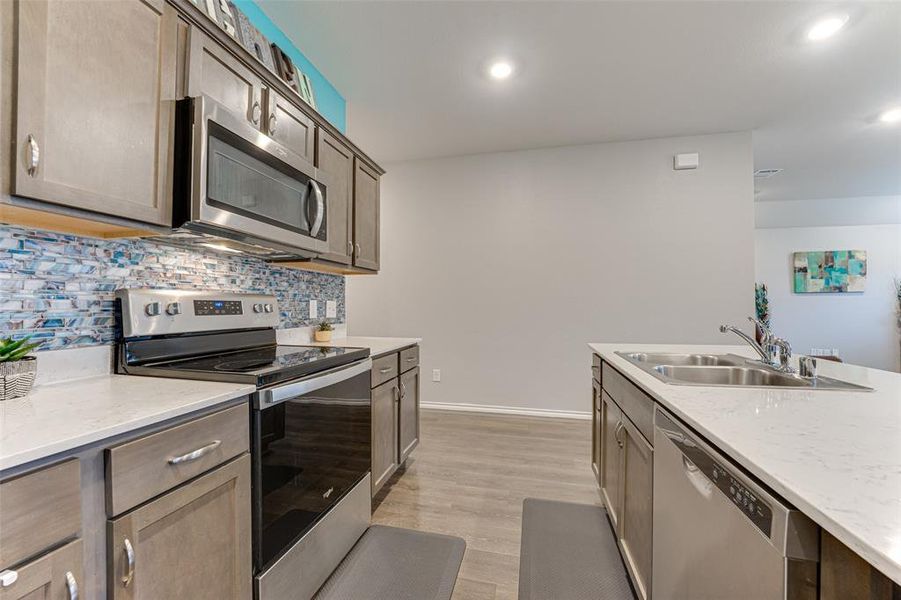 Kitchen with sink, light stone counters, backsplash, light hardwood / wood-style floors, and appliances with stainless steel finishes