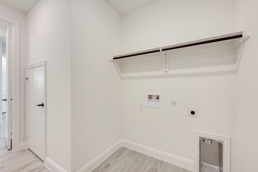 Laundry room with wall shelf, washer hookups, dryer outlet, and pet door on light wood-look tile floor Laundry room with wall shelf, washer hookups, dryer outlet, and pet door on light wood-look tile floor