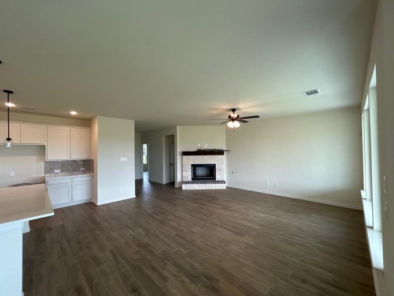 Spacious open-concept interior featuring wood-finish flooring, a built-in fireplace with a tile surround and wood mantel, and ceiling fan