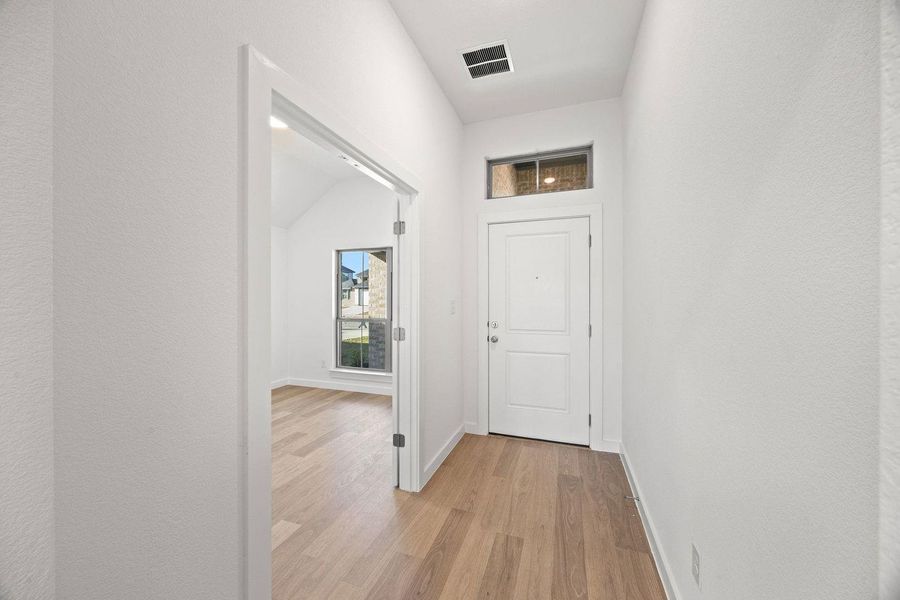 Enter into a hallway featuring wood flooring and a modern entryway with a transom window.