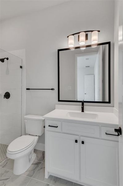 Bathroom featuring tiled shower, vanity, and toilet