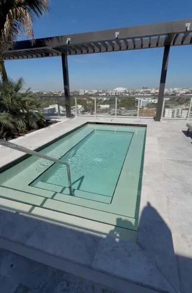 Rooftop plunge pool featuring natural stone tiling, a metal pergola, a glass panel railing, and integrated metal handrail