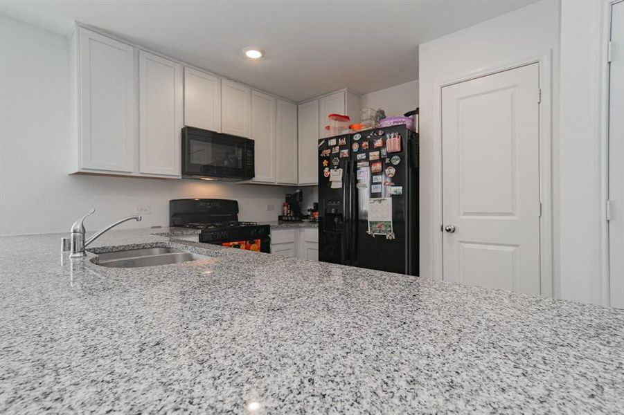 Kitchen with light stone countertops, black appliances, white cabinets, and recessed lighting