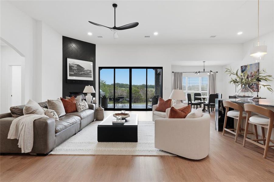 Expansive open-concept living area featuring wood-finish flooring, a vaulted ceiling with a modern ceiling fan, and a black accent wall with a mounted television