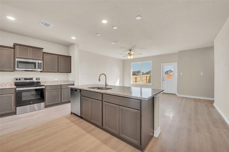 Kitchen with stainless steel appliances, an island with sink, light stone counters, light wood finished floors, and open floor plan