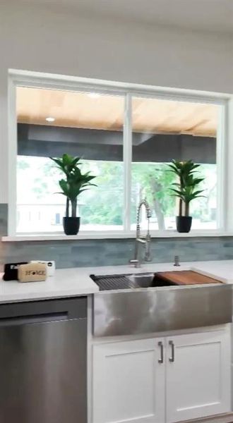 Modern kitchen featuring a stainless steel farmhouse sink with a gooseneck faucet, white shaker cabinetry, stainless steel dishwasher, light-toned countertops, and a subway tile backsplash