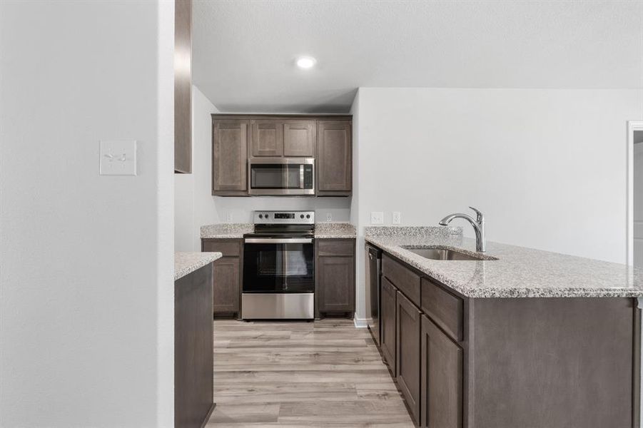 Kitchen with stainless steel appliances, light hardwood / wood-style floors, sink, light stone counters, and kitchen peninsula