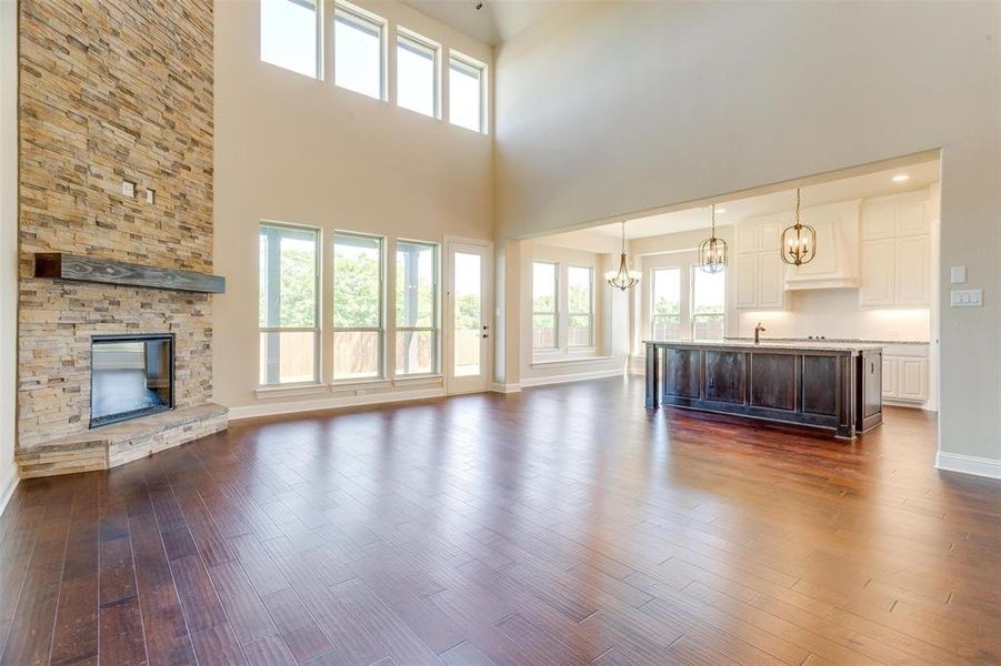 Unfurnished living room with a high ceiling, a stone fireplace, dark wood-type flooring, and a chandelier