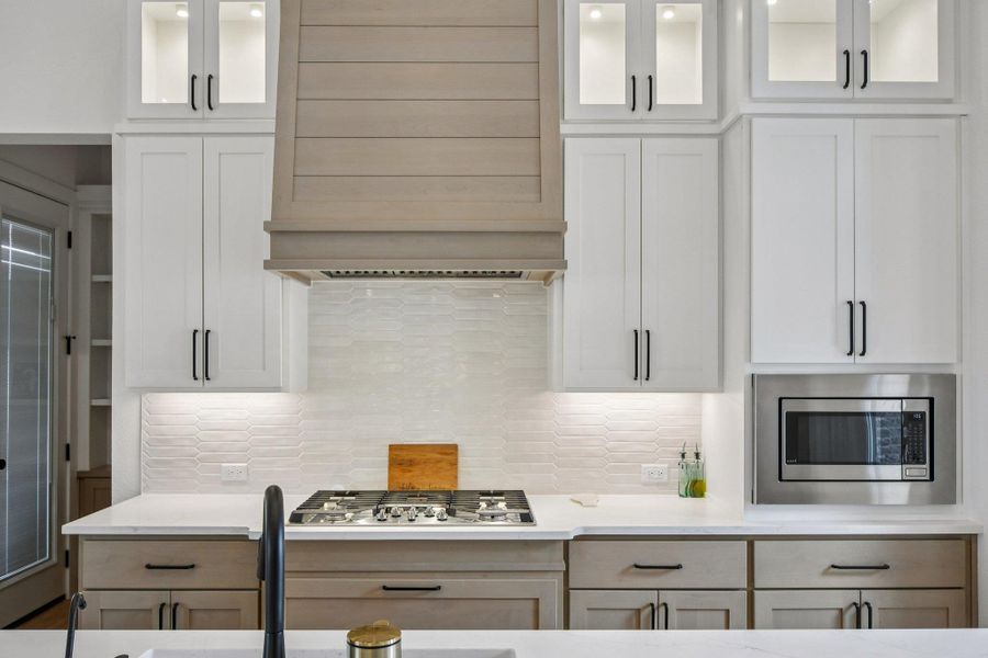 The kitchen features a gas range with a decorative range hood, white shaker-style cabinetry, and a built-in stainless steel microwave The kitchen features a gas range with a decorative range hood, white shaker-style cabinetry, and a built-in stainless steel microwave