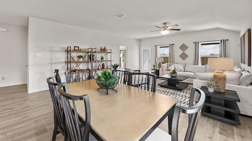 This open concept living space features light-toned flooring, a light-colored dining table with dark chairs, and a living area with a ceiling fan