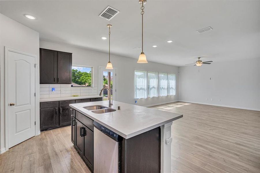 Kitchen featuring light hardwood / wood-style flooring, sink, decorative backsplash, a kitchen island with sink, and dishwasher