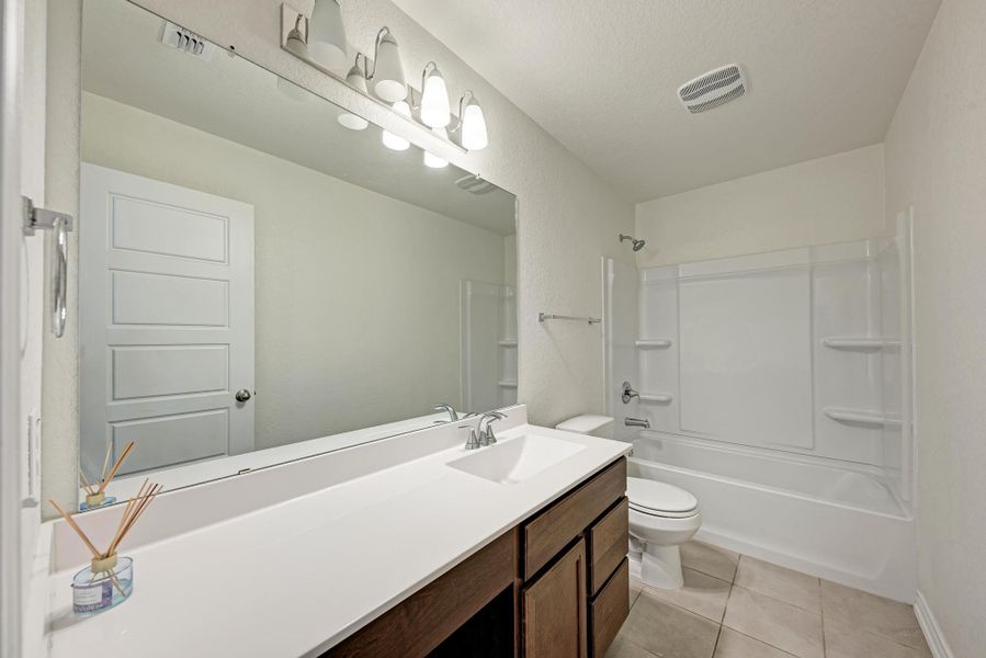A pristine bathroom features a single vanity, large mirror, and a combined tub and shower.