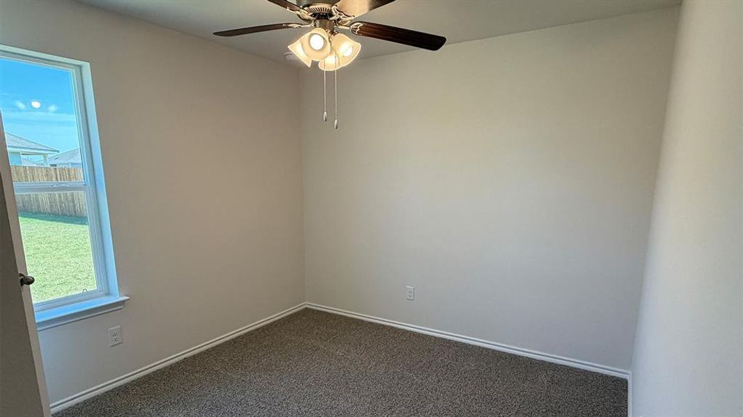 Unfurnished room with dark colored carpet and a ceiling fan