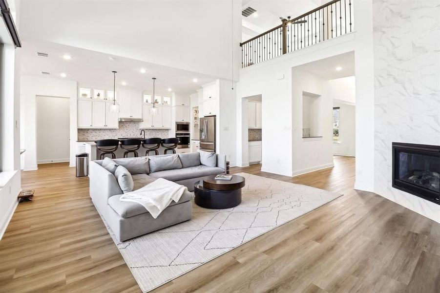 Living area featuring a fireplace, light wood-style floors, recessed lighting, a towering ceiling, and a chandelier Living area featuring a fireplace, light wood-style floors, recessed lighting, a towering ceiling, and a chandelier