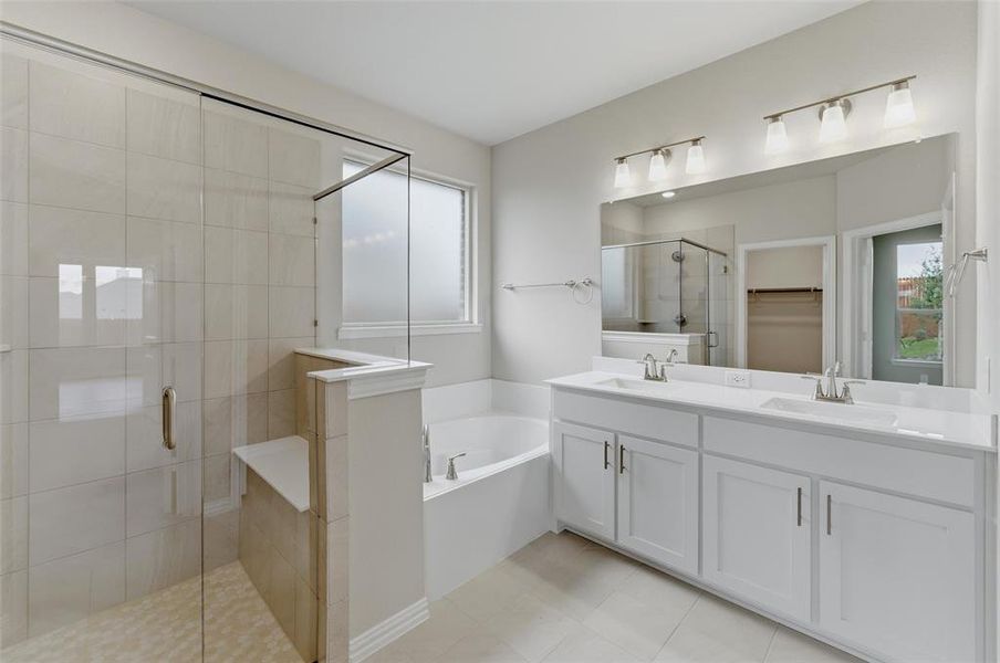 Spacious bathroom featuring a dual vanity with white cabinetry, a large frameless mirror, a tiled walk-in shower with a built-in bench, a separate soaking tub, and neutral-toned tile flooring