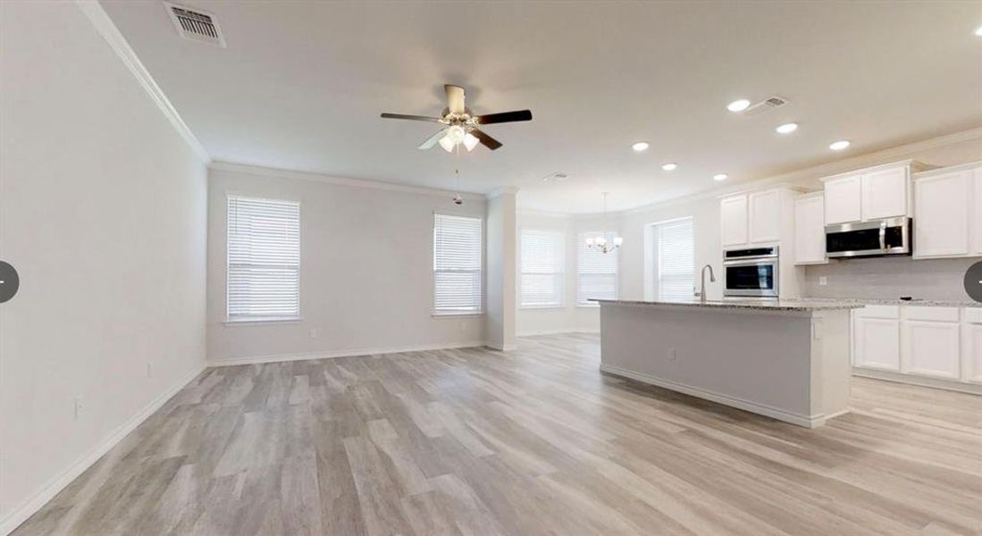Kitchen with appliances with stainless steel finishes, crown molding, open floor plan, a chandelier, and light wood-type flooring