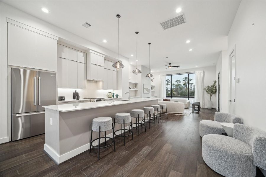 Expansive island anchors the heart of the home, offering generous prep space, breakfast bar seating, and seamless integration with the living and dining areas. High ceilings, recessed lighting, and modern pendant fixtures complement the sleek cabinetry and stainless appliances, delivering both sophistication and practicality in this thoughtfully designed open layout.