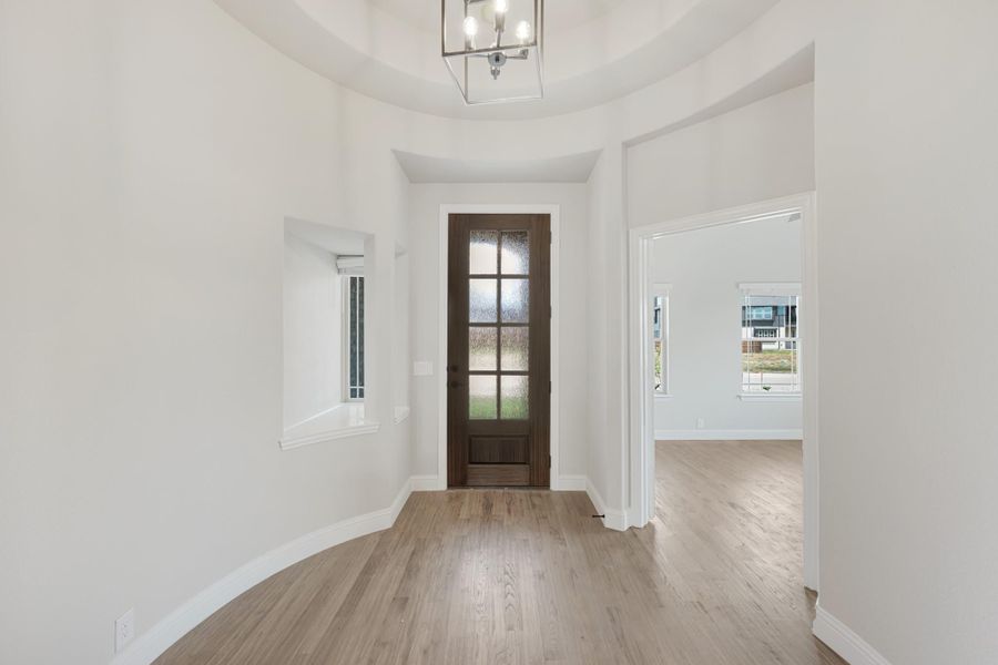 Foyer with round tray ceiling, wood front door with glass panels, chandelier, and light hardwood floors Foyer with round tray ceiling, wood front door with glass panels, chandelier, and light hardwood floors