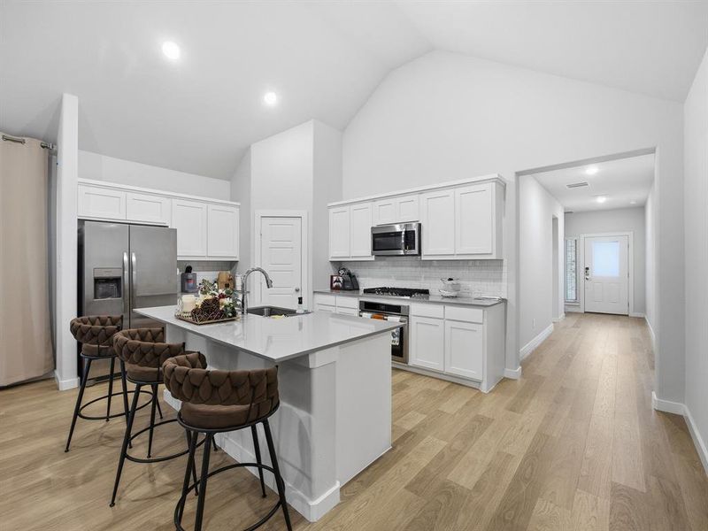 Kitchen featuring decorative backsplash, white cabinets, light wood-type flooring, appliances with stainless steel finishes, and a breakfast bar area