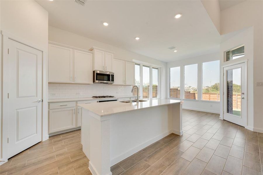 Kitchen with white cabinets, sink, an island with sink, and a healthy amount of sunlight