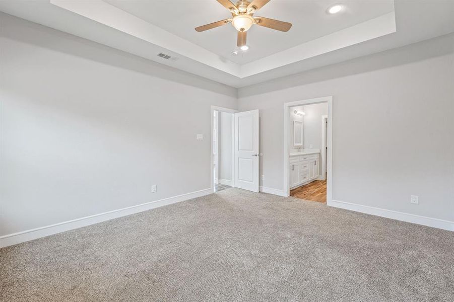 Unfurnished bedroom with a tray ceiling, light carpet, ensuite bath, a ceiling fan, and recessed lighting Unfurnished bedroom with a tray ceiling, light carpet, ensuite bath, a ceiling fan, and recessed lighting