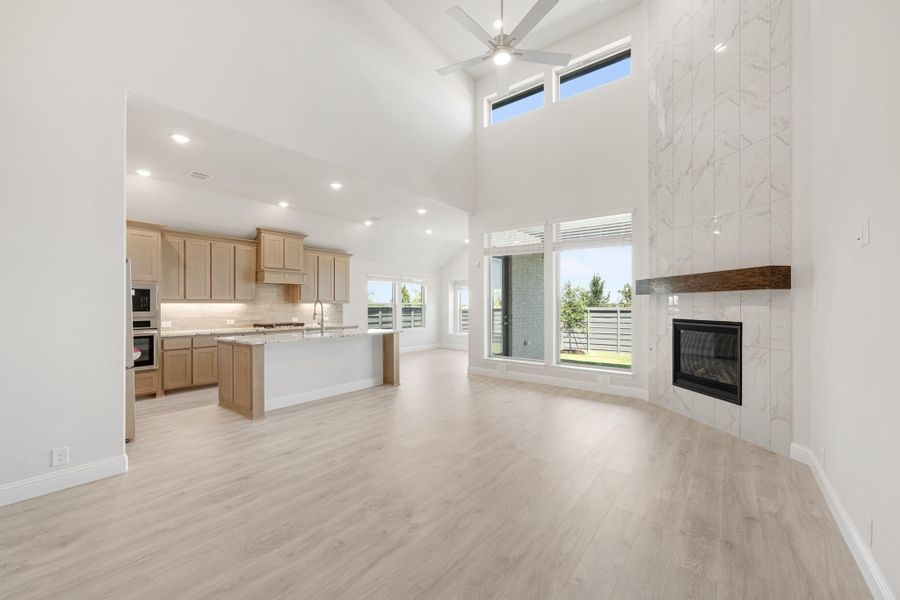 Open living area with high ceilings, marble fireplace, and kitchen with island and light wood cabinets