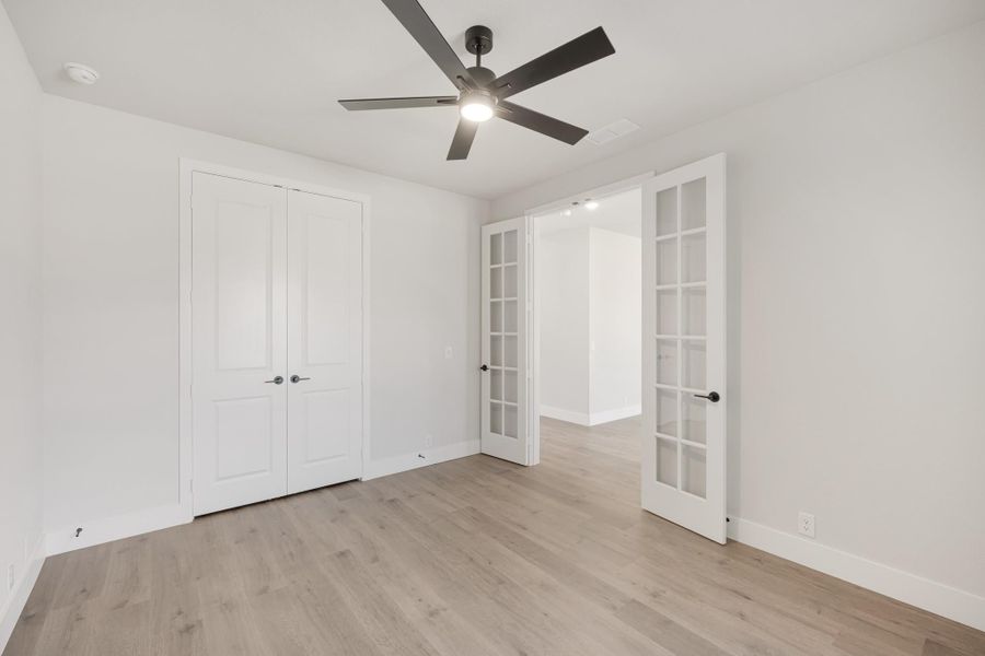 Empty bedroom with hardwood floors, ceiling fan, closet, and white French doors Empty bedroom with hardwood floors, ceiling fan, closet, and white French doors