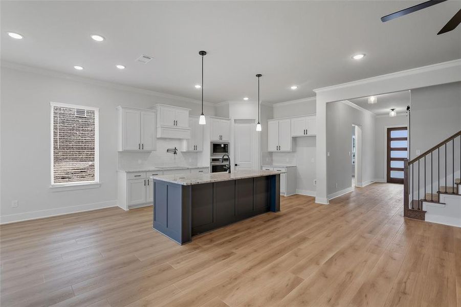 Dual tone kitchen with a center island with sink, decorative light fixtures, two tone color scheme, light stone counters, and ornamental molding
