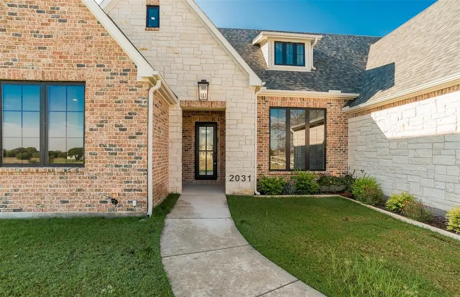 Entrance to property featuring a shingled roof, a lawn, and brick siding