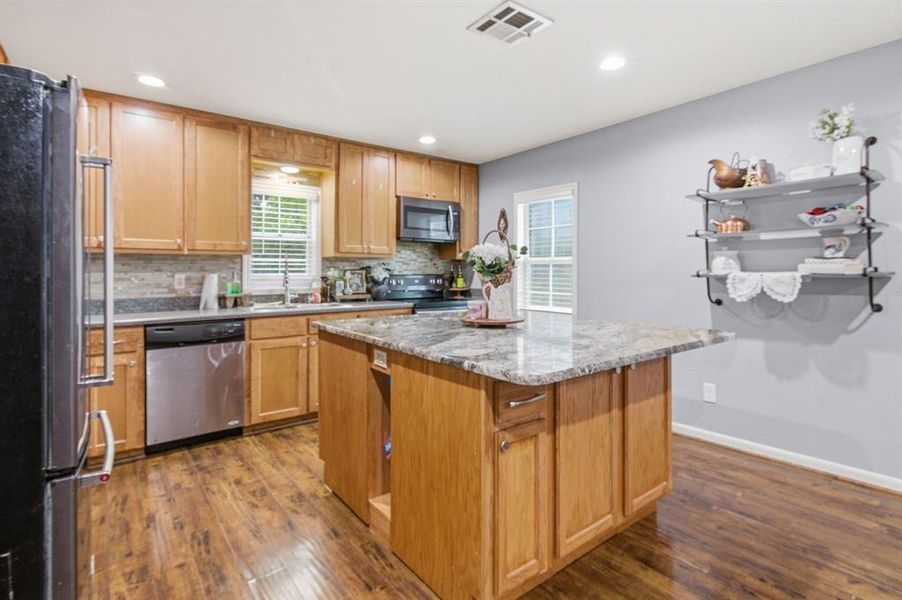 Kitchen featuring wood-finish flooring, a central island with a stone countertop, wood cabinetry, stainless steel appliances, and recessed lighting