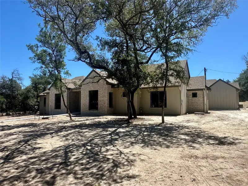 Mature oak trees frame a modern single-story stone exterior under clear blue skies.