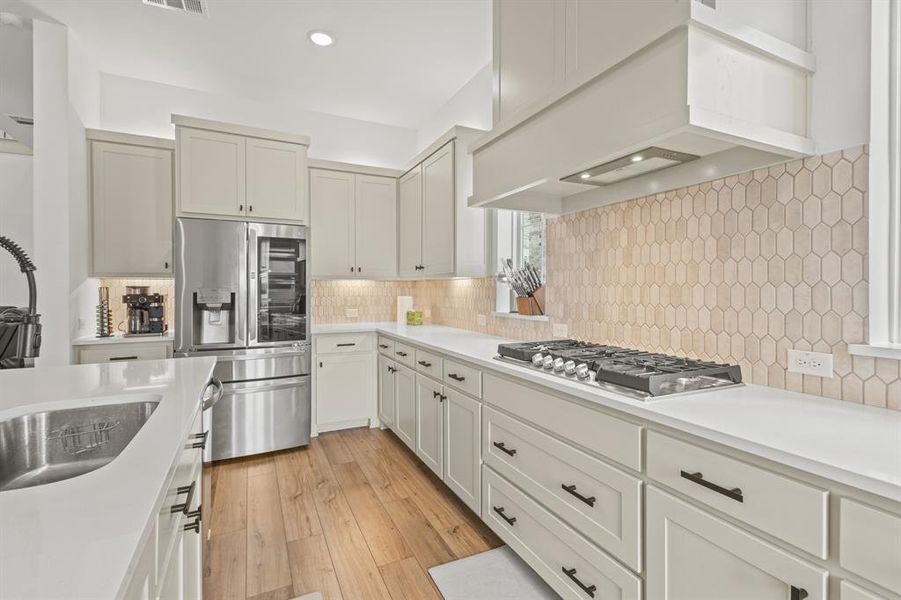 Kitchen featuring custom range hood, stainless steel appliances, light wood-style floors, decorative backsplash, and recessed lighting