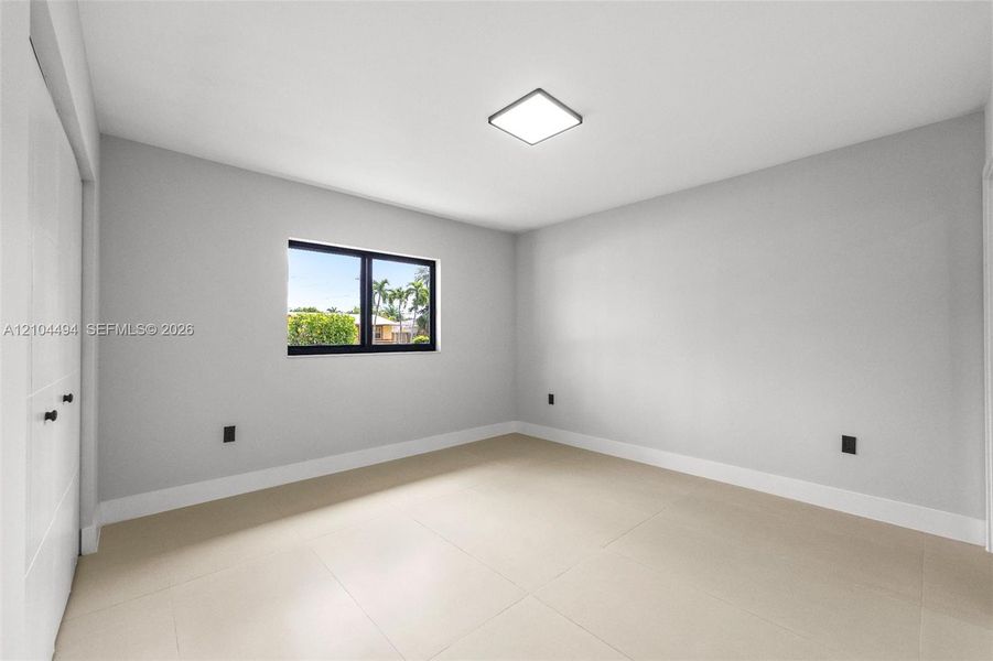 Neutral-toned interior featuring large-format tile flooring, recessed square ceiling lighting, and a window with a black frame