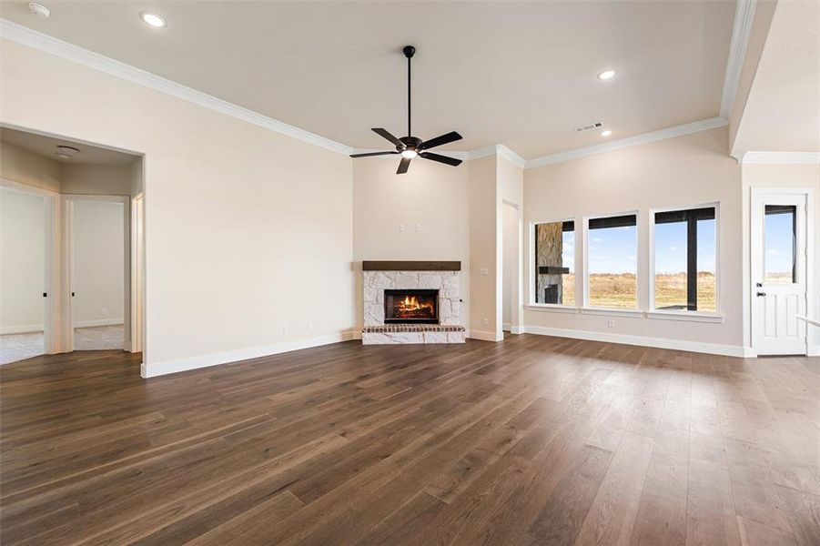 Unfurnished living room with ornamental molding, a stone fireplace, dark wood finished floors, recessed lighting, and ceiling fan
