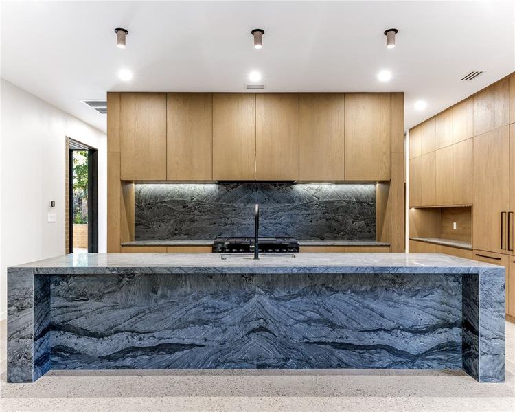 Kitchen featuring Wakanda quartzite countertops and backsplash, custom modern cabinets, exposed aggregate flooring, an island with sink, and recessed lighting.