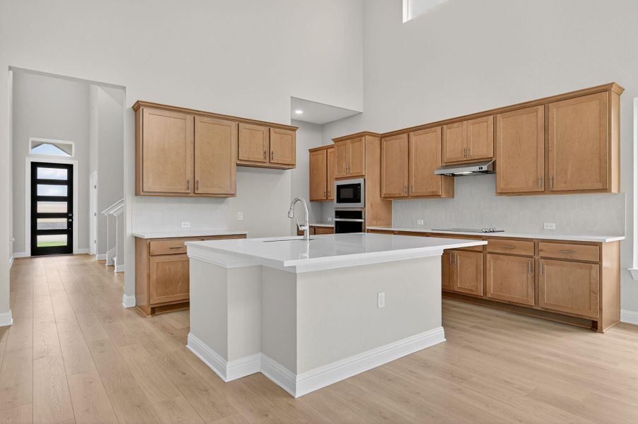 Kitchen featuring a kitchen island with sink, oven, a towering ceiling, light wood-type flooring, and built in microwave