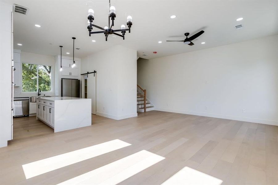 Unfurnished living room featuring a barn door, a chandelier, stairs, recessed lighting, and light wood-style floors