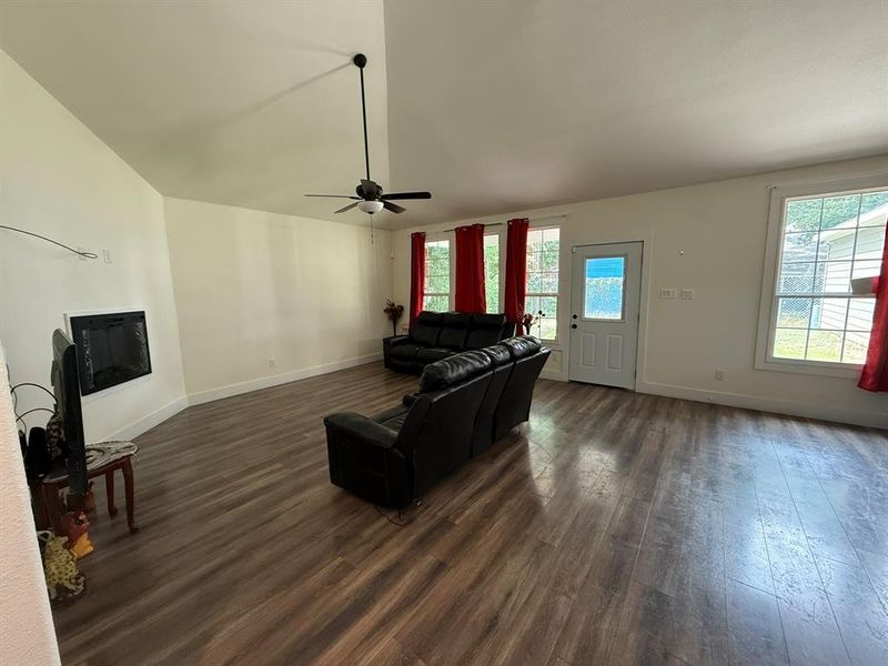 Living room with lofted ceiling, dark wood-style flooring, a glass covered fireplace, and ceiling fan