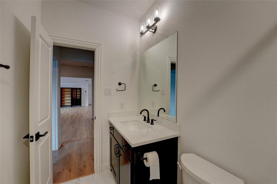 Half bathroom with vanity, vinyl finished floors, and toilet