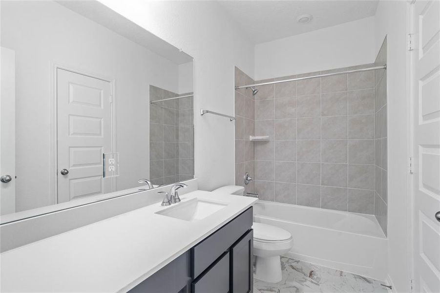 Secondary bath features tile flooring, bath/shower combo with tile surround, stained wood cabinets, beautiful light countertops, mirror, sleek fixtures and modern finishes.