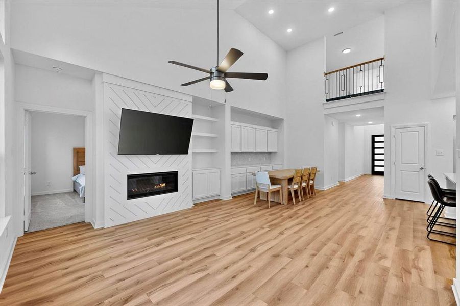 Living room with recessed lighting, high vaulted ceiling, light wood finished floors, a large fireplace, and ceiling fan Living room with recessed lighting, high vaulted ceiling, light wood finished floors, a large fireplace, and ceiling fan