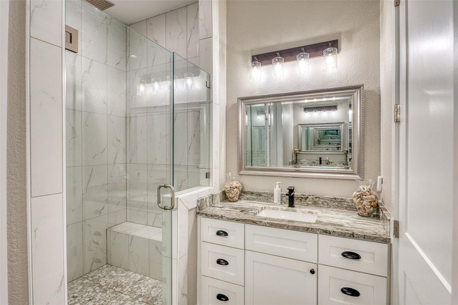 Bathroom featuring a marble finish shower, vanity, and a textured wall