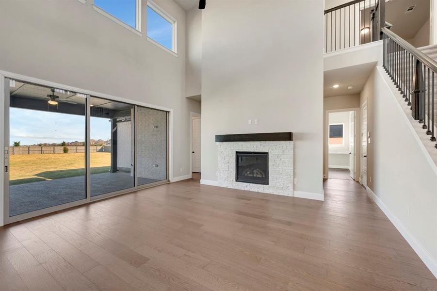 Unfurnished living room with wood finished floors, a high ceiling, a stone fireplace, and a ceiling fan Unfurnished living room with wood finished floors, a high ceiling, a stone fireplace, and a ceiling fan