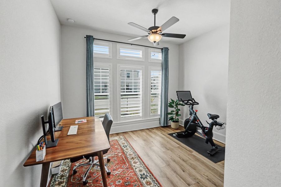 This bright downstairs secondary space features plantation shutters and durable flooring. It is currently configured as a home gym and secondary workspace.