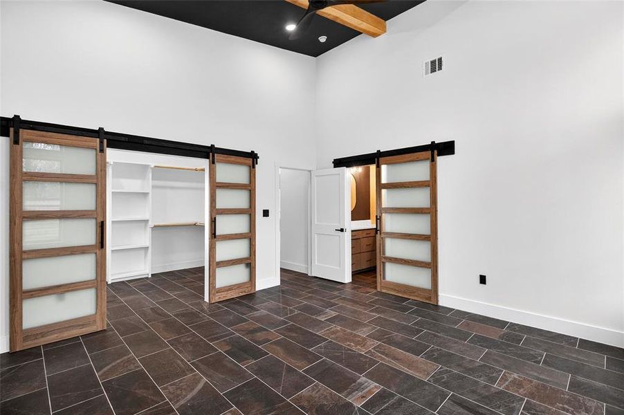 Unfurnished bedroom with a barn door, a high ceiling, ensuite bath, and a walk in closet Unfurnished bedroom with a barn door, a high ceiling, ensuite bath, and a walk in closet