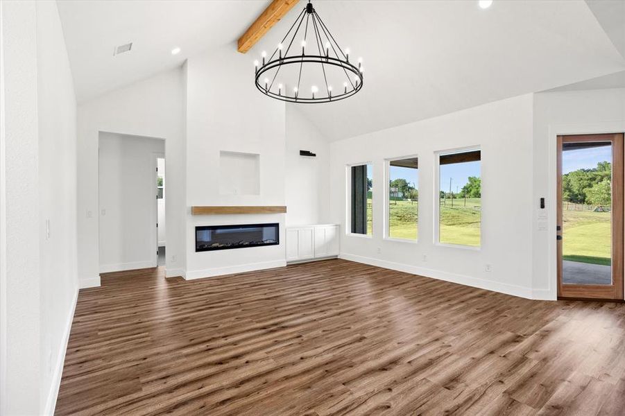 Unfurnished living room featuring high vaulted ceiling, dark wood-style floors, beam ceiling, a glass covered fireplace, and recessed lighting Unfurnished living room featuring high vaulted ceiling, dark wood-style floors, beam ceiling, a glass covered fireplace, and recessed lighting