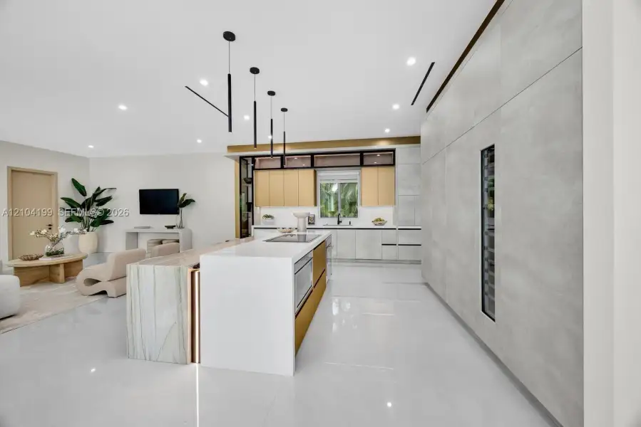 Kitchen featuring a central island with waterfall-edge countertop, floor-to-ceiling cabinetry with integrated beverage storage, matte metallic base accents, and linear pendant lighting